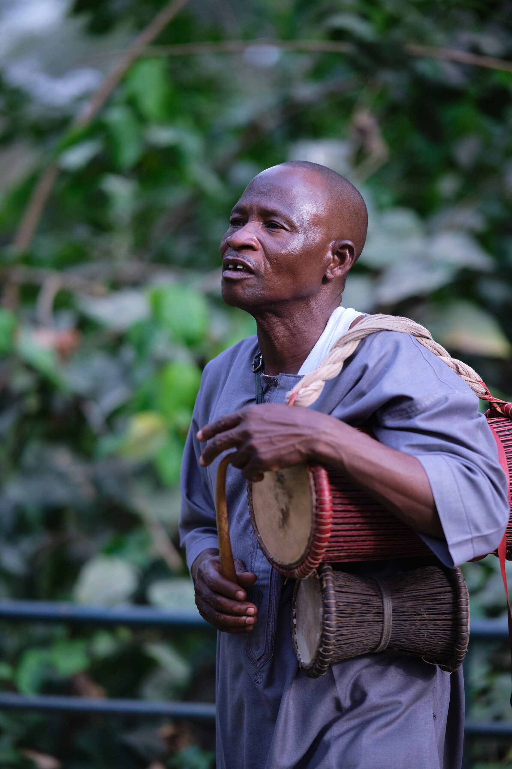 A Yoruba musician performing on an hourglass-shaped dùndún talking drum with a curved beater